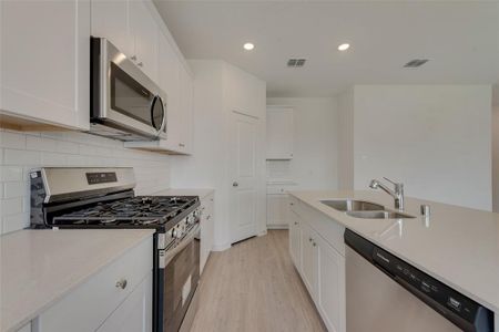 Kitchen with stainless steel appliances, white cabinets, light hardwood / wood-style floors, and sink