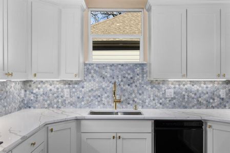 Kitchen with black dishwasher, sink, backsplash, white cabinets, and light stone counters