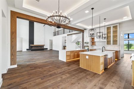 Kitchen with decorative light fixtures, dark wood-type flooring, an island with sink, and backsplash