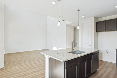 Kitchen with hanging light fixtures, a kitchen island with sink, light wood-type flooring, sink, and light stone counters