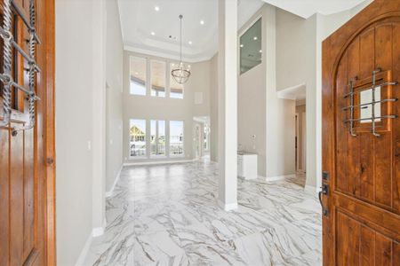 This is a spacious, bright entryway with high ceilings, elegant marble flooring, and a view through to a back patio. A statement wooden door adds a touch of warmth to the modern design.