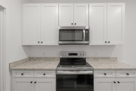 Kitchen featuring stainless steel appliances, white cabinetry, and light stone counters