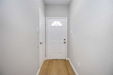 This is a bright, welcoming entryway featuring a white door with an arched window, neutral walls, and wood-look tile flooring.