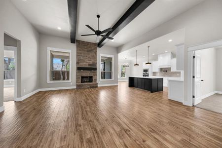 Unfurnished living room with beamed ceiling, ceiling fan, a fireplace, and light wood-type flooring