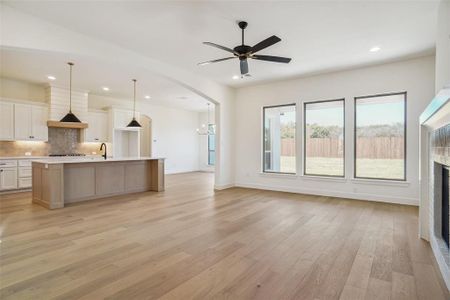 Kitchen with a large island, hanging light fixtures, a brick fireplace, light hardwood / wood-style floors, and white cabinets