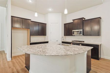 Kitchen featuring a center island with sink, dark brown cabinets, pendant lighting, and sink