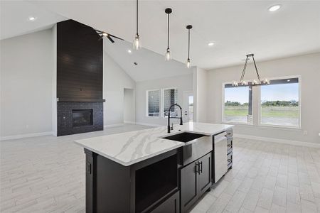 Kitchen with sink, stainless steel dishwasher, an island with sink, pendant lighting, and a fireplace