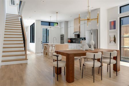 Kitchen with hanging light fixtures, light hardwood / wood-style flooring, stainless steel appliances, white cabinets, and backsplash