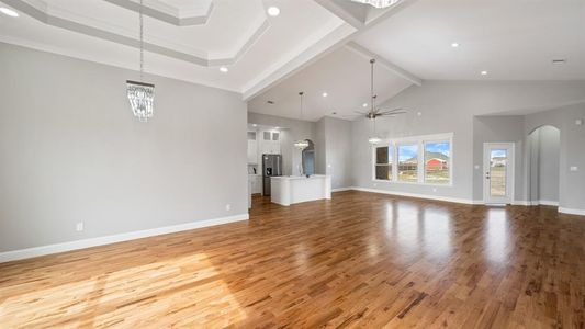 Unfurnished living room featuring arched walkways, beam ceiling, light wood finished floors, baseboards, and ceiling fan with notable chandelier