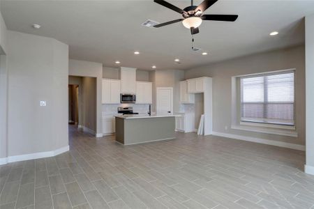 Kitchen featuring an island with sink, white cabinets, ceiling fan, stainless steel appliances, and backsplash