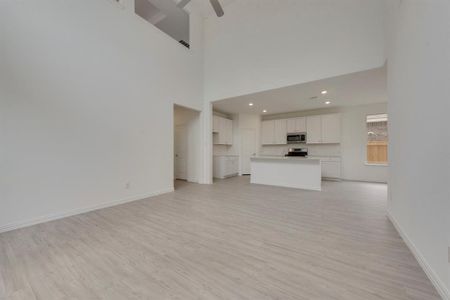 Unfurnished living room featuring ceiling fan, light wood-type flooring, and a towering ceiling