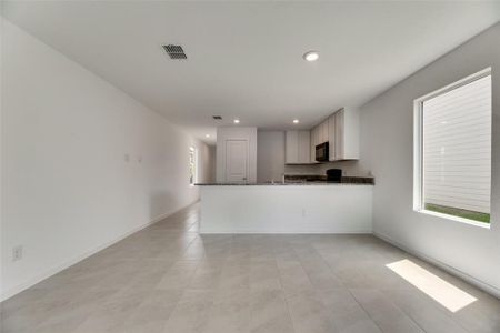 Kitchen with kitchen peninsula, light tile patterned flooring, white cabinets, and dark stone countertops