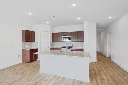 Kitchen with light stone countertops, backsplash, an island with sink, light hardwood / wood-style floors, and appliances with stainless steel finishes