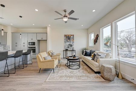 This bright, modern living area features an open layout with a sleek kitchen, bar seating, and a cozy living space. Large windows provide ample natural light, while neutral tones create a welcoming atmosphere.