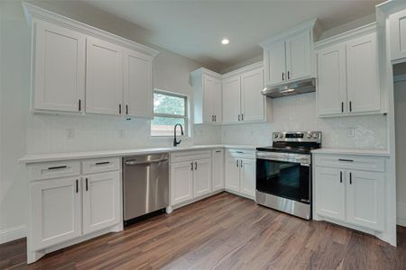 Kitchen with stainless steel appliances, sink, white cabinets, and dark hardwood / wood-style flooring