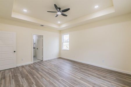 Unfurnished bedroom with ensuite bath, ceiling fan, hardwood / wood-style flooring, and a tray ceiling