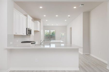 Kitchen featuring kitchen peninsula, decorative backsplash, white cabinetry, light wood-type flooring, and sink