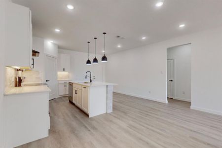 Kitchen with white cabinets, stove, sink, decorative light fixtures, and a kitchen island with sink