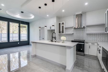 Kitchen featuring white cabinetry, sink, wall chimney exhaust hood, hanging light fixtures, and stainless steel stove