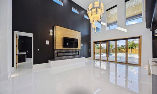 This is a modern living space featuring high ceilings, a contrasting color scheme with dark walls and white floors, a built-in fireplace area, and large windows that provide plenty of natural light and a view of the outdoor pool area.