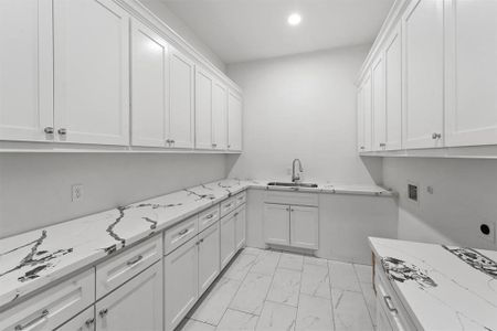 This is a sleek modern kitchen featuring white cabinetry with ample storage and marble-like countertops, complemented by a clean, minimalist design.