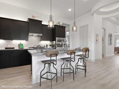 Kitchen with a kitchen bar, backsplash, pendant lighting, a center island with sink, and light hardwood / wood-style flooring