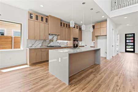 Kitchen with light hardwood / wood-style flooring, a center island with sink, decorative light fixtures, backsplash, and appliances with stainless steel finishes