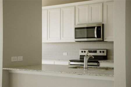 Kitchen featuring decorative backsplash, white cabinetry, stove, and light stone countertops