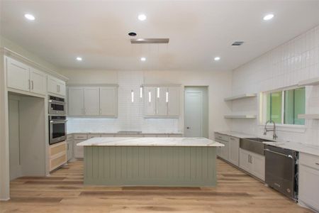 Kitchen featuring tasteful backsplash, light hardwood / wood-style flooring, stainless steel appliances, a center island, and sink