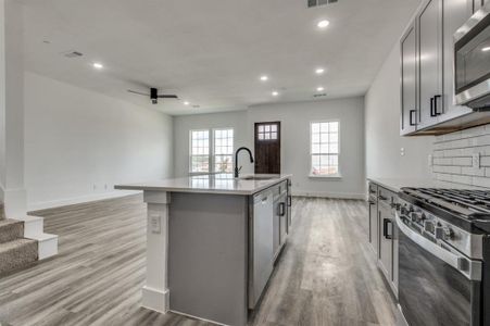 Kitchen with gray cabinetry, a center island with sink, stainless steel appliances, sink, and light hardwood / wood-style floors