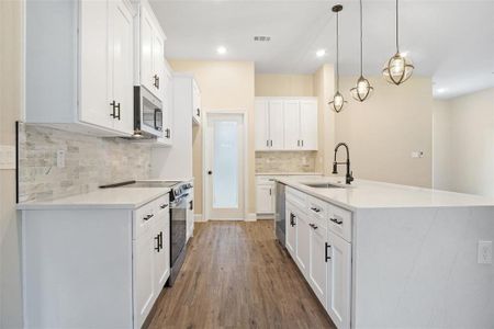 Kitchen with backsplash, hardwood / wood-style flooring, hanging light fixtures, stainless steel appliances, and sink