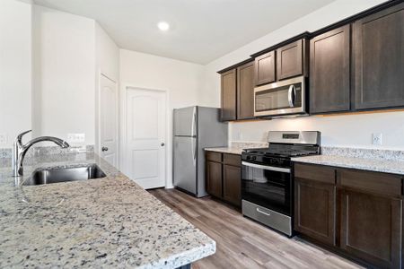 Kitchen featuring dark brown cabinets, light hardwood / wood-style floors, light stone countertops, appliances with stainless steel finishes, and sink