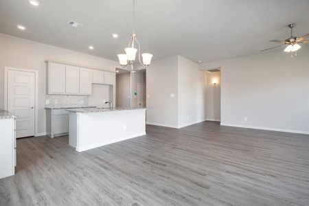 Kitchen with white cabinets, an island with sink, tasteful backsplash, decorative light fixtures, and light hardwood / wood-style floors