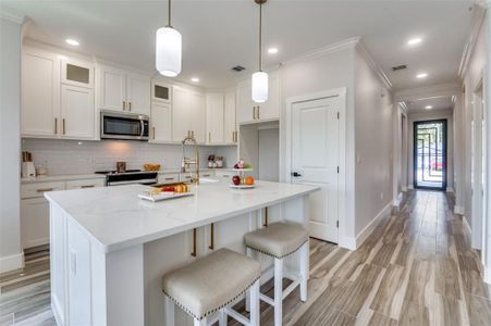 Kitchen featuring range with electric cooktop, tasteful backsplash, a kitchen island with sink, white cabinets, and crown molding