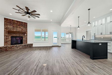 Kitchen with light hardwood / wood-style floors, ceiling fan with notable chandelier, a brick fireplace, and tasteful backsplash