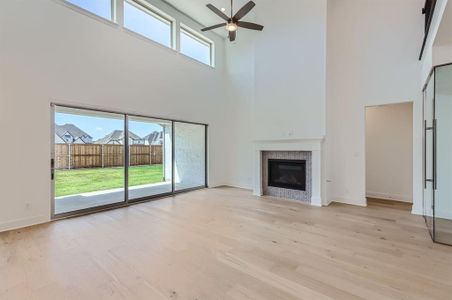 Unfurnished living room featuring a high ceiling, a tiled fireplace, a wealth of natural light, and ceiling fan