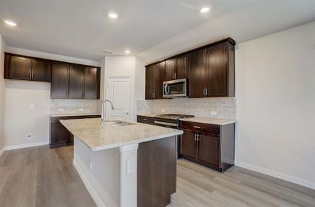 Kitchen with light hardwood / wood-style flooring, tasteful backsplash, light stone countertops, sink, and a center island with sink