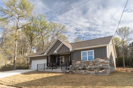 View of front of property with stone siding, driveway, an attached garage, and roof with shingles