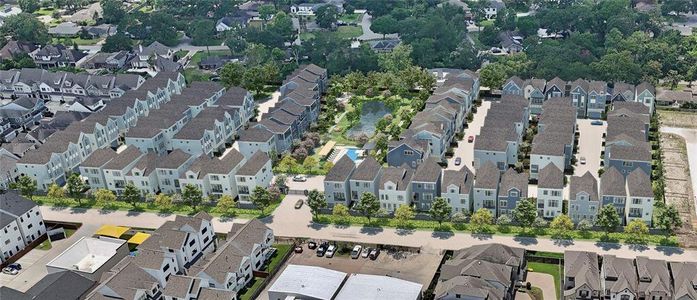 This aerial photo showcases a well-planned residential community featuring rows of modern homes with uniform architecture. The area includes landscaped green spaces and a central pool, offering a blend of urban living and nature. It's a serene neighborhood with easy access to surrounding amenities.