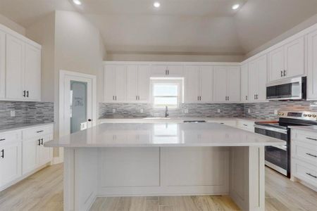 Kitchen featuring a center island, vaulted ceiling, appliances with stainless steel finishes, white cabinets, and a sink