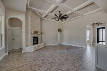 Unfurnished living room featuring a stone fireplace, coffered ceiling, a towering ceiling, beamed ceiling, and ceiling fan