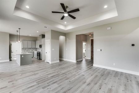 Unfurnished living room featuring sink, light hardwood / wood-style flooring, ceiling fan, and a tray ceiling