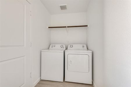 Clothes washing area with light wood-type flooring and separate washer and dryer