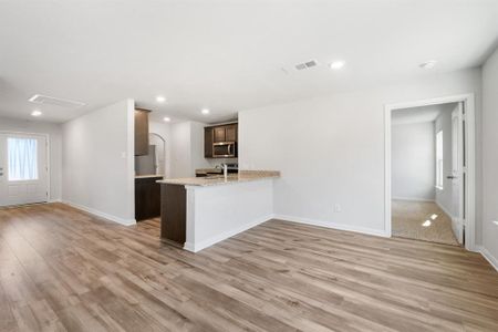 Kitchen featuring kitchen peninsula, light hardwood / wood-style flooring, light stone counters, and dark brown cabinetry