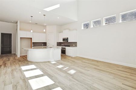 Kitchen with a high ceiling, a center island with sink, light wood-type flooring, appliances with stainless steel finishes, and white cabinetry