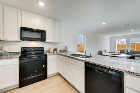 Kitchen featuring light hardwood / wood-style floors, light stone counters, kitchen peninsula, black appliances, and white cabinetry