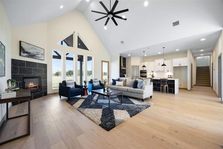 Living room with a tile fireplace, light wood-type flooring, high vaulted ceiling, and ceiling fan