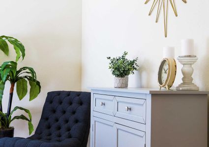 Staged model with a clock on a desk, plants and a dark blue chair.