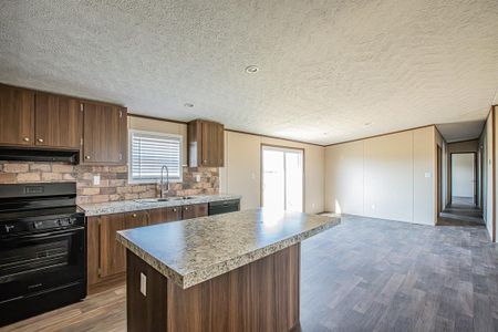 Kitchen featuring a textured ceiling, black appliances, a kitchen island, dark wood-type flooring, and sink