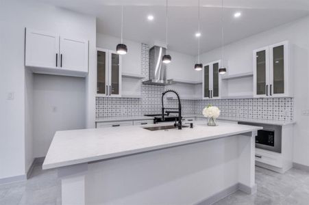 Kitchen featuring pendant lighting, wall chimney exhaust hood, white cabinetry, and sink